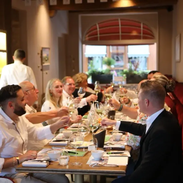 Un groupe de personnes assises autour d'une table dans un restaurant, partageant un repas et des discussions, avec des verres de vin et des petits bols devant eux