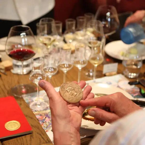 Une personne tient une médaille dorée devant une table avec des verres de vin et des documents