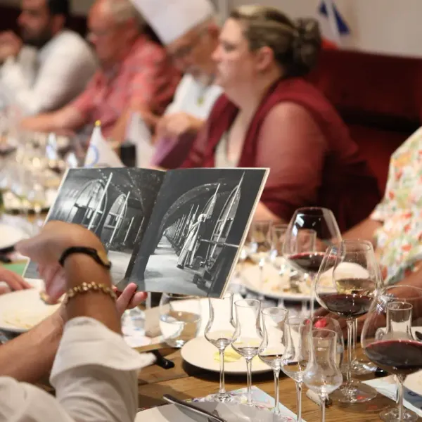 Un groupe de personnes assises autour d'une table avec des verres de vin, examinant une image en noir et blanc
