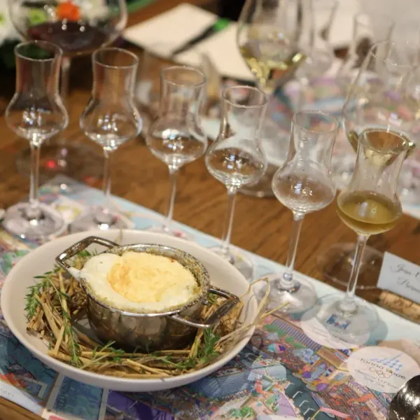 Une table avec plusieurs verres de vin et un plat contenant une préparation culinaire entourée de fines herbes