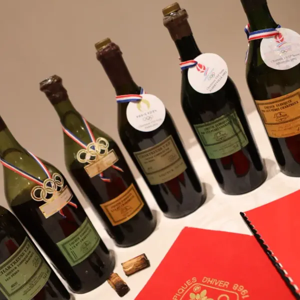 Une collection de bouteilles de vin et de spiritueux avec des étiquettes commémoratives des Jeux Olympiques et des médailles, disposées sur une table