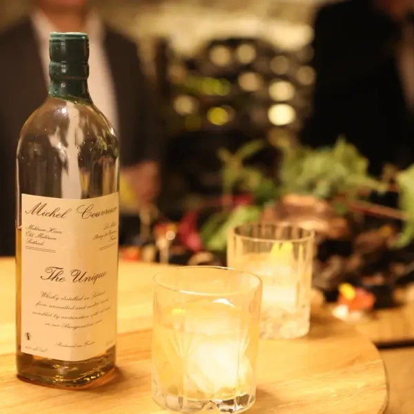 Bouteille de whisky Michel Couvreur "The Unique" posée sur une table en bois avec deux verres à whisky