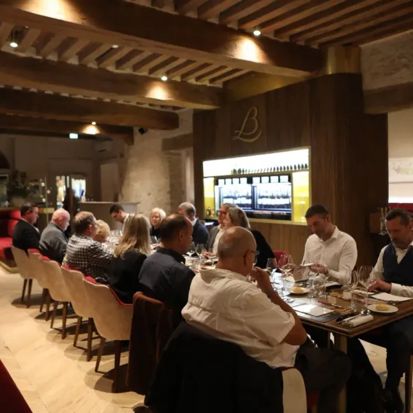 Un groupe de personnes est assis autour de tables dans un restaurant à la décoration rustique, discutant et dégustant des plats
