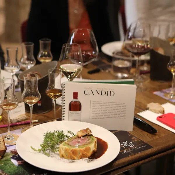 Table garnie de verres à vin, d'une bouteille et d'une assiette avec une préparation culinaire, accompagnée de notes et d'un téléphone portable