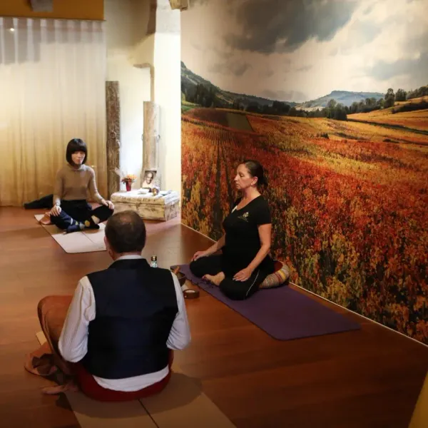 Un groupe de personnes pratique la méditation dans une salle avec un grand paysage mural représentant des champs