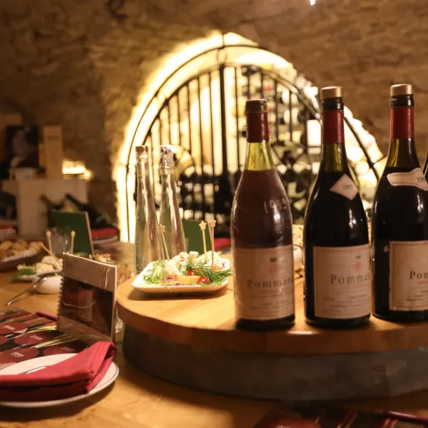 Bouteilles de vin et assiette de nourriture sur une table en bois dans une cave à vin éclairée