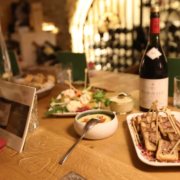 Table dressée avec des plats variés, une bouteille de vin et des verres, dans un cadre éclairé par des lumières tamisées