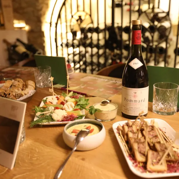 Bouteille de vin Pommard sur une table avec divers plats et verres dans un caveau à vin