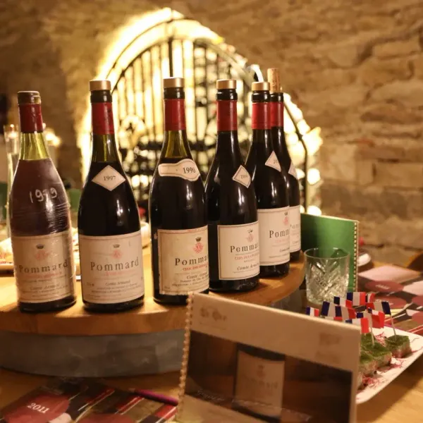 Bouteilles de vin Pommard de différentes années disposées sur une table en bois avec des verres et des assiettes