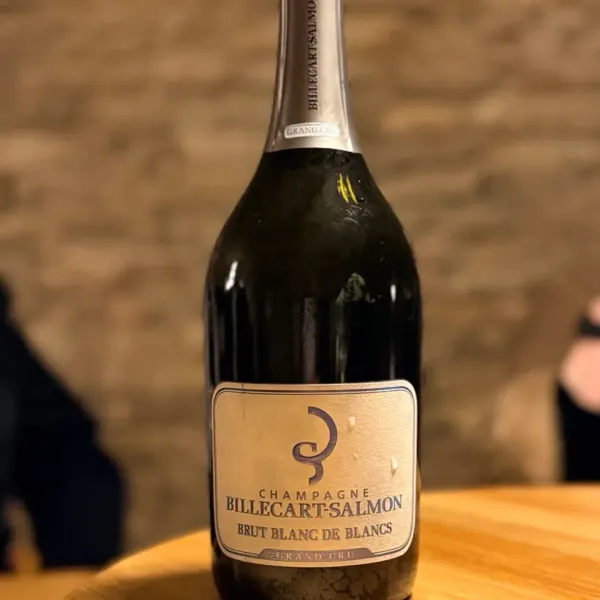 Bouteille de champagne Billecart-Salmon Brut Blanc de Blancs Grand Cru posée sur une table en bois devant un mur de pierre