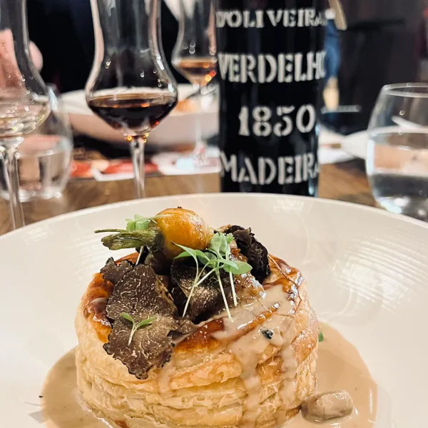 Un plat gastronomique avec une tarte fine garnie de truffes et d'un jaune d'œuf, accompagné de deux verres de vin et d'une bouteille de vin de Madère